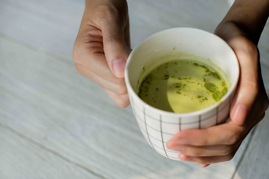 Seseorang sedang memegang secangkir teh matcha berwarna hijau terang